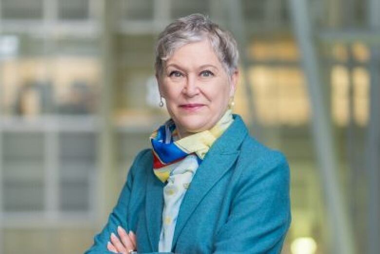 A silver-haired woman stands with arms crossed.