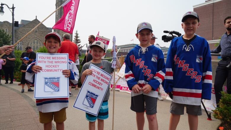 A group of kids wearing hockey jerseys hold signs at a rally.