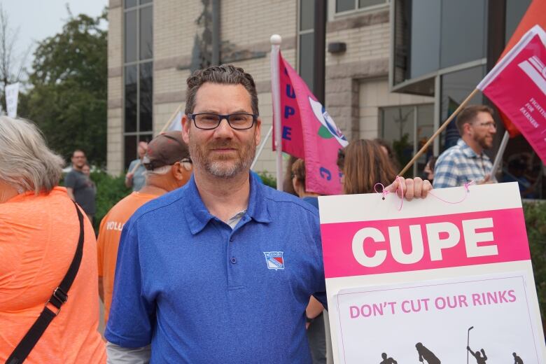 A man wearing glasses holds a sign at rally outside Thunder Bay City Hall.