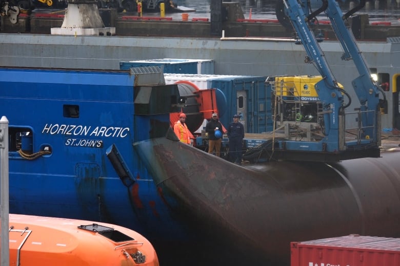 A yellow square-shaped machine sits on the right side of a blue ship. 