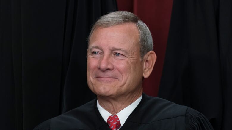 A clean-shaven man is shown in closeup wearing a judicial robe over a collared shirt and tie.