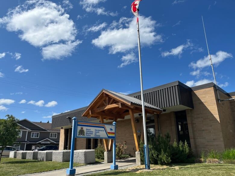 A Canadian flag flies above a sign with the name and insignia of the RCMP, in front of a small brick building that serves as the RCMP detachment in Vanderhoof. 