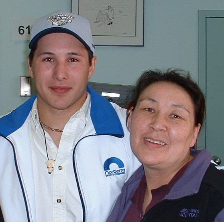 A young man in a baseball hat poses with a middle-aged woman.