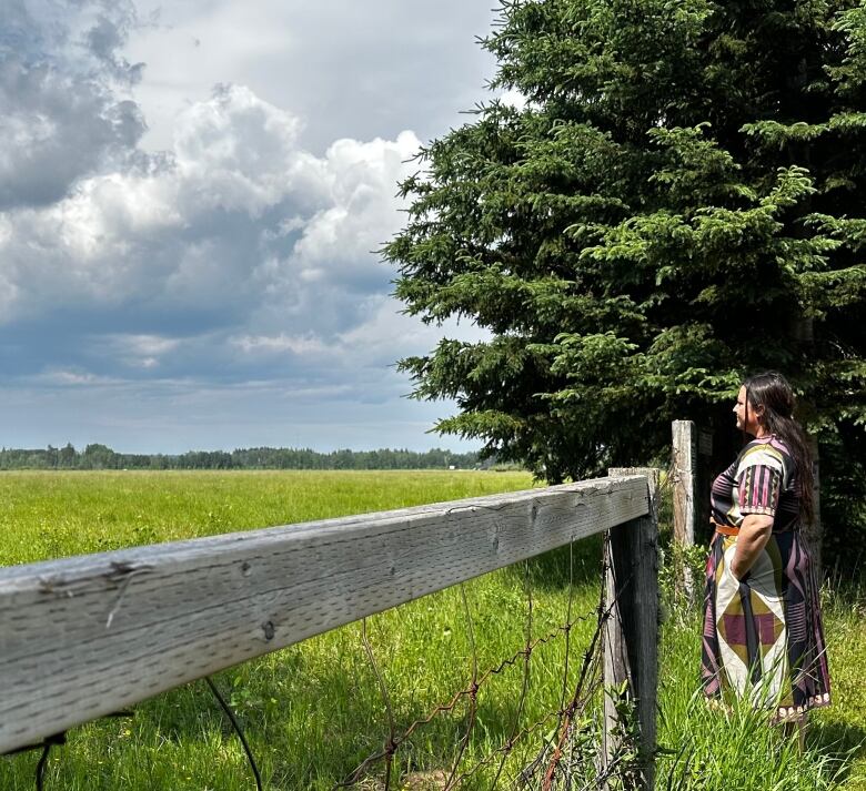 A woman with long, dark hair in a colourful dress looks out onto a section of Rocky Mountain House National Historic Site, where she helped coordinate a successful backburn last summer. 