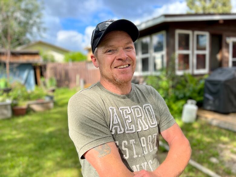 A smiling man in a ball cap stands in a yard.