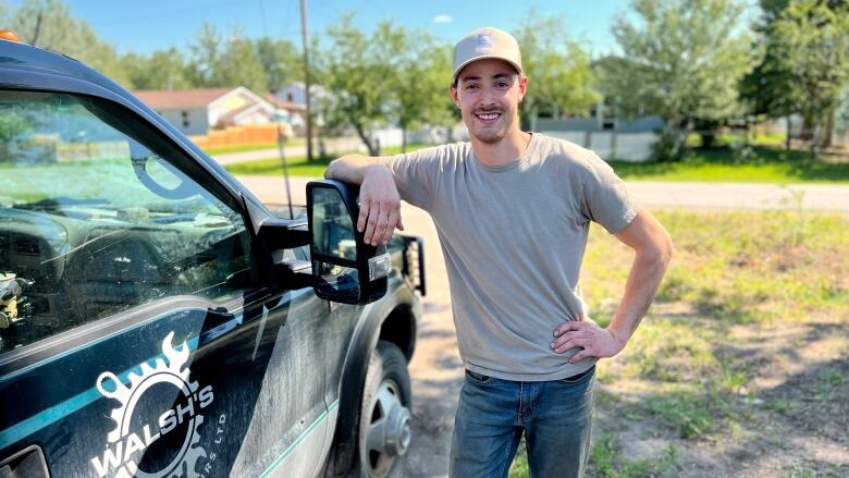 A young man smiles and leans on a truck.