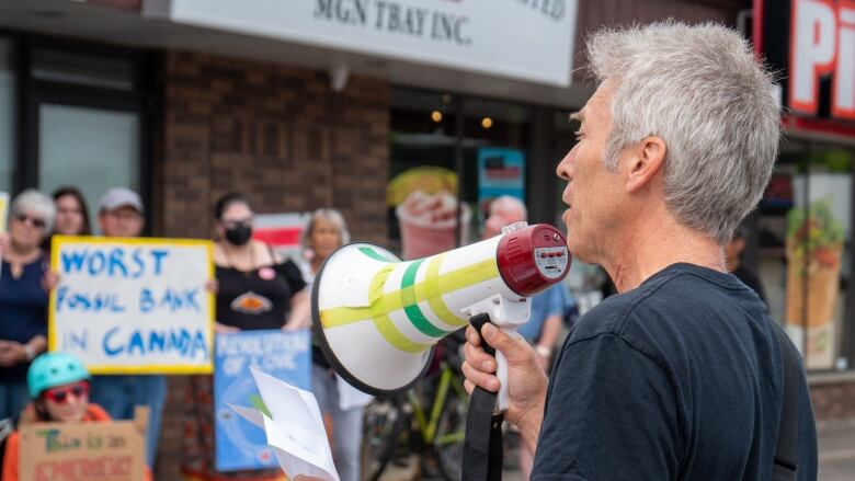 A man with a  megaphone stands outside in front of a crowd of people.