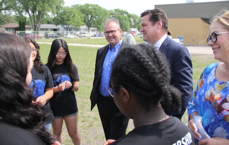 MLAs and students stand in a circle and talk amongst themselves. 