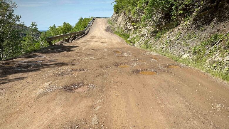 A gravel road with very little gravel and a lot of potholes leads up a hill.