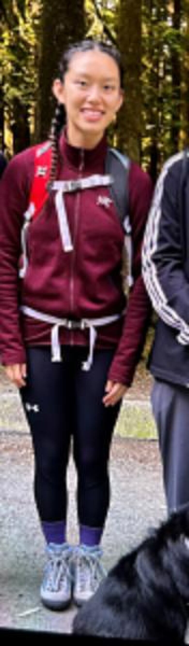 A young Asian teenaged girl wearing black leggings, a maroon jacket and a backpack.