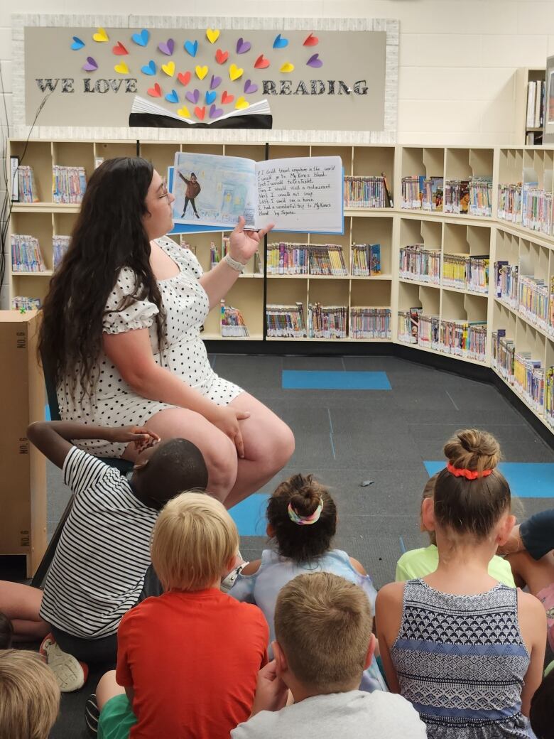 Kids watch their teacher read a book in a library