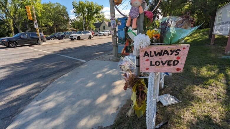 A white-painted bike is adorned with flowers and a sign that says 