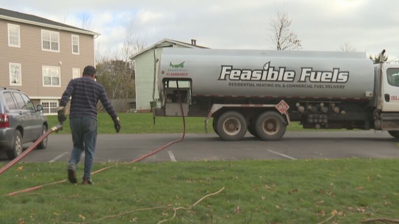 A man drags a fuel hose back to a tanker truck with the logo Feasible Fuels on the side. 