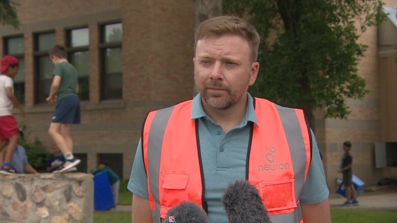 Isaac Ransom stands with a bright orange vest on in front of a school building.