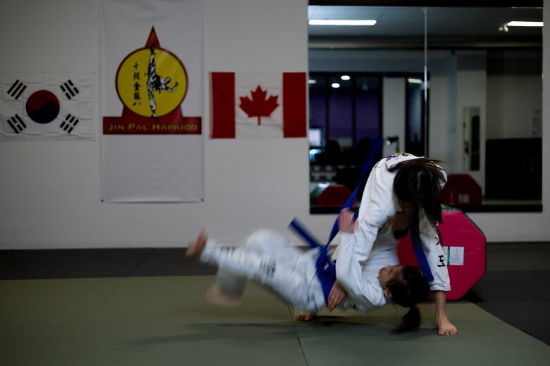 A young girl in a gi flips another onto the ground of a dojang. 