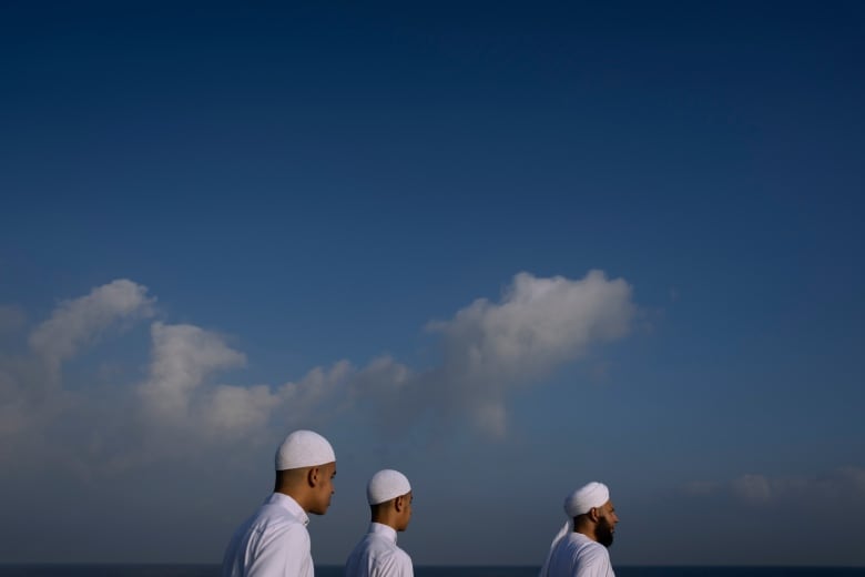 Three men walk in front of a blue sky in Israel.