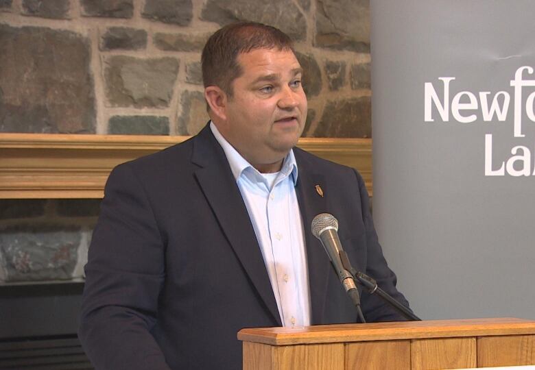 A man in a suit stands in front of a podium.