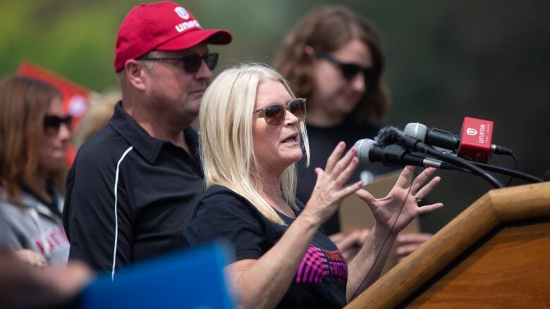 A woman in a black t-shirt speaks at a podium.