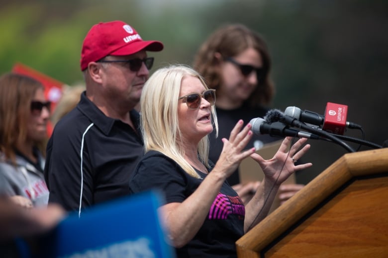 A woman in a black t-shirt speaks at a podium.