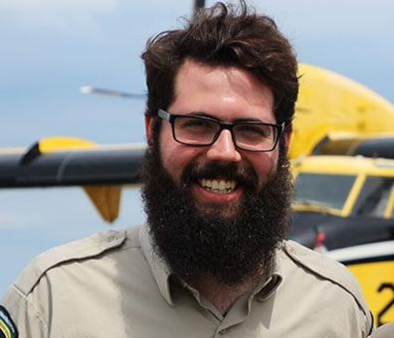 Man with beard stands in front of plane. 