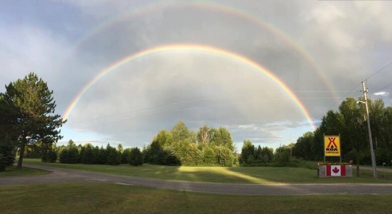 Campground sign on grassy lawn with a double rainbow overhead. 