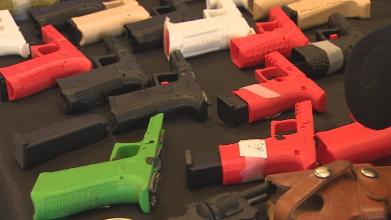 Several 3D printed guns sit on a table. They are different colours, black, green and red.