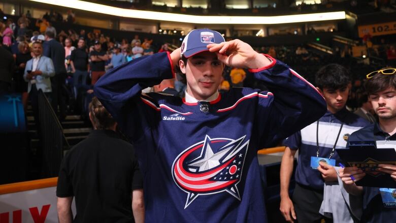 A man wears a blue hockey jersey in front of a stage