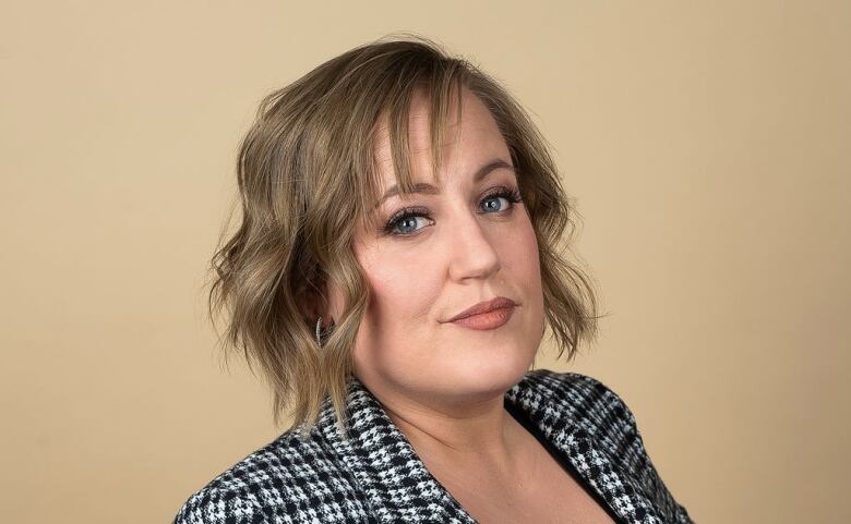 A woman with short, brownish hair wears a checked blazer. 