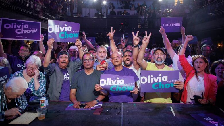 Supporters holding Olivia Chow for Mayor signs fill a room at an election nigh event.