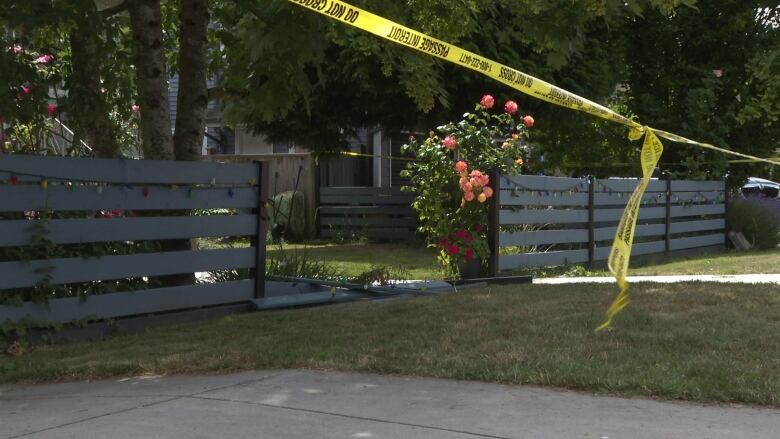 A yard with a fence behind police tape, with one section of fence collapsed.