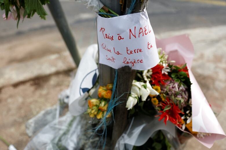 Bouquests of flowers lean against a pole. A message above them reads: 