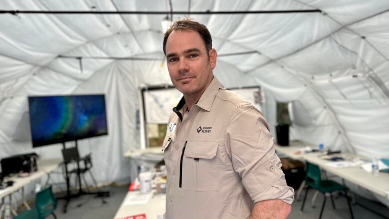 A man wearing a beige shirt stands in the middle of a white tent with a rounded top.