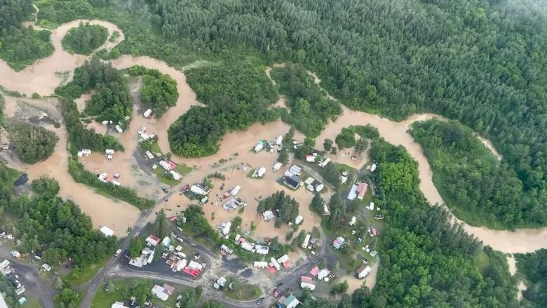 An aerial view of a small city that is partially flooded, with flooded forested areas to the north.