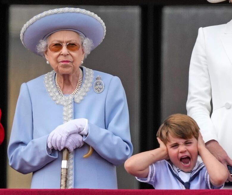 A child holds their hands over their ears as they stand beside an adult.