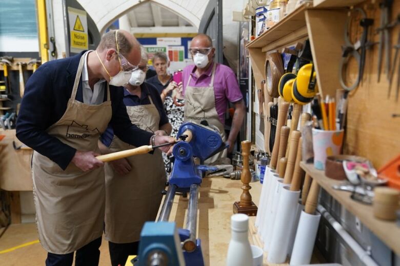 A person uses a lathe as other people watch.