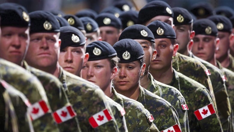 Male and female members of the Canadian Armed Forces march in a lineup wearing green CADPAT uniforms and black berets.