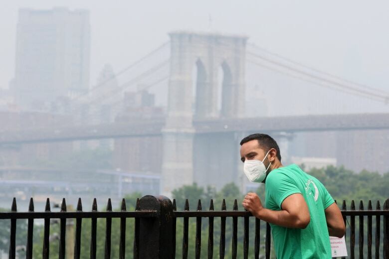 A man wears a mask while looking at lower Manhattan shrouded in haze and smoke from wildfires in Canada from the Brooklyn Promenade in New York City, U.S., June 30, 2023. 