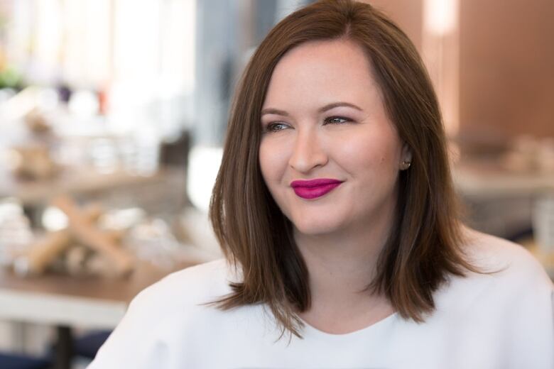 Woman in white shirt looks off camera in front of blurred, bright area.