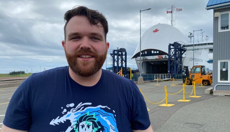 A man in a t-shirt stands in front of a ferry docked in a wharf.