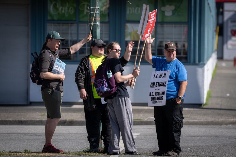 A group of men holding placards wave at a location off-camera.