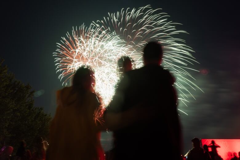 Fireworks explode as the silhouettes of people looking on are seen in the foreground.