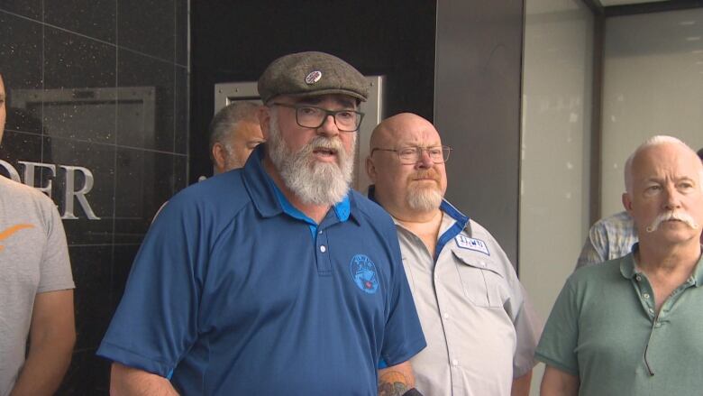 A man in a cap with blue shirt speaks surrounded by other men wearing ILWU union shirts.