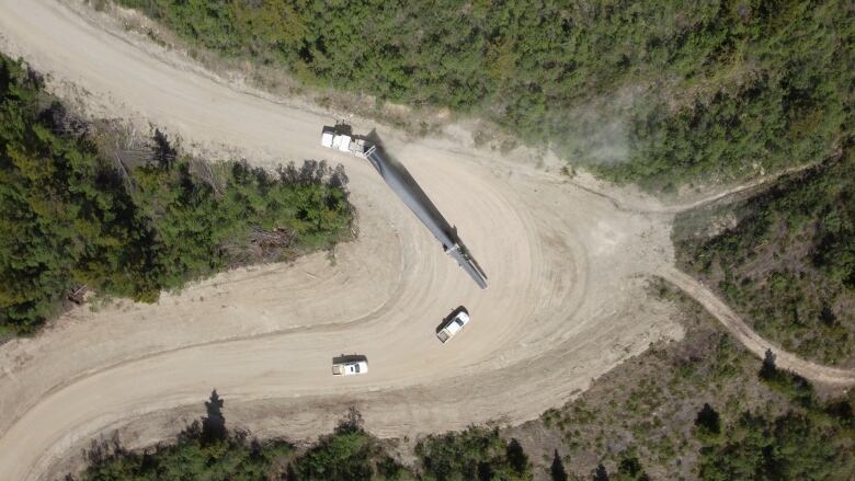 An aerial photo looking down on a transport truck carrying a wind turbine blade on a winding dirt road.