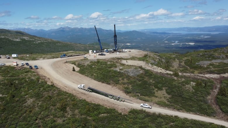 Aerial shot of a transport truck going up a mountain road toward two construction cranes working on a hilltop.