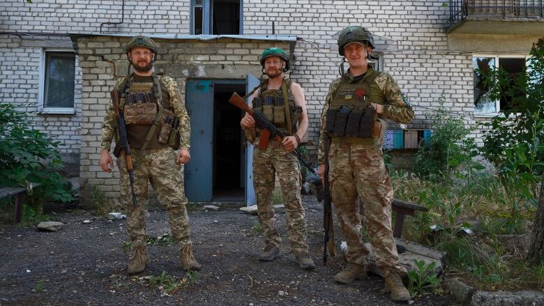 Three Ukrainian soldiers stand outside an apartment block.