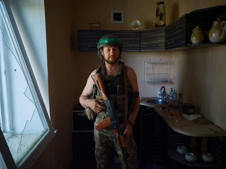 A Ukrainian soldier stands in a room with a rifle.