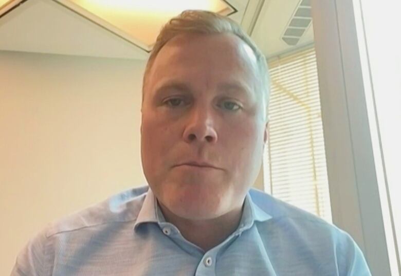 A head-and-shoulders shot of a man with blond hair and a light blue dress shirt