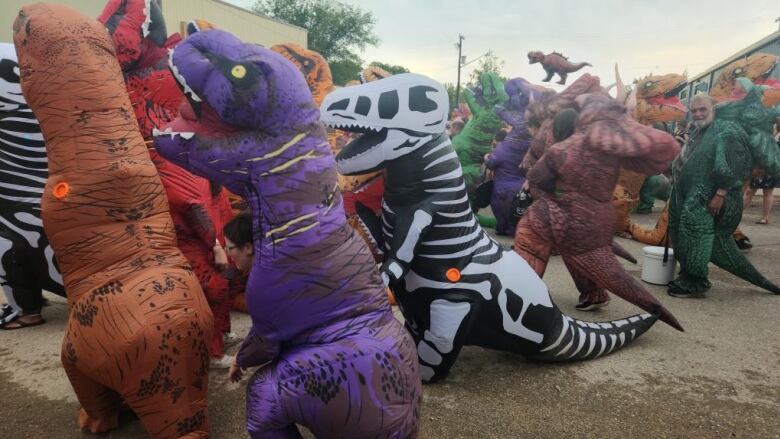 People are in inflatable dinosaur costumes on a street in dundurn.