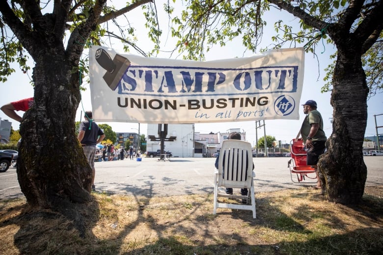 A large sign strung up between two trees reads 