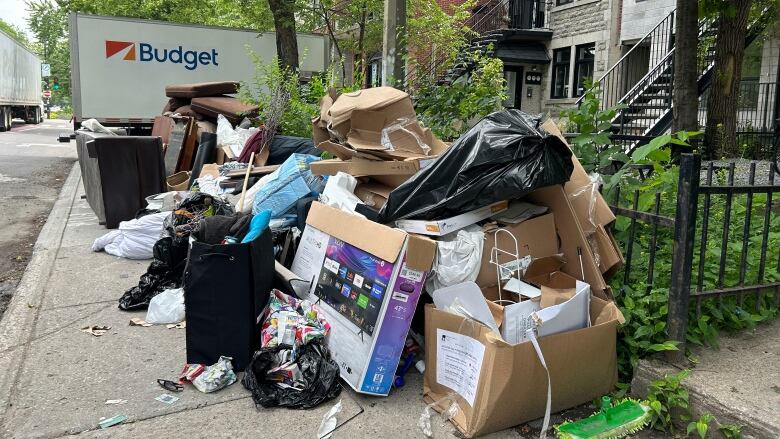 A large pile of junk, including a mop head, a tv box and other mangled garbage bags and boxes sits on a sidewalk in Montreal's Plateau neighbourhood.